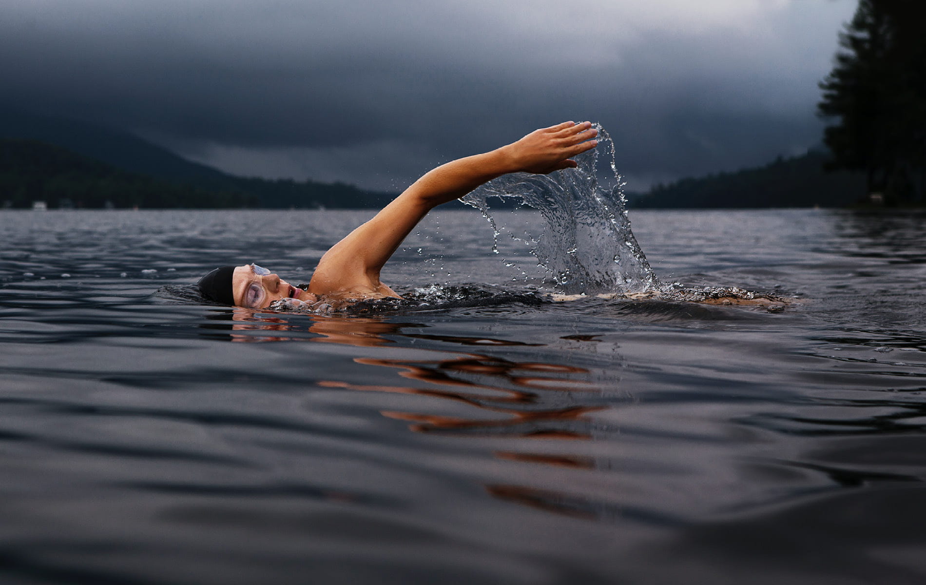 Mann schwimmt mit Taucherbrille und Badekappe im See