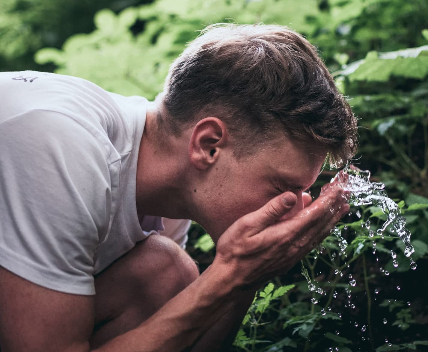 Mann wäscht sich das Gesicht mit Wasser in der Natur | Biohacking