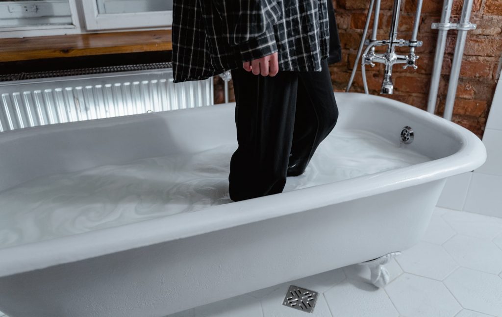 Person steht mit Hose in mit Wasser gefüllten Badewanne