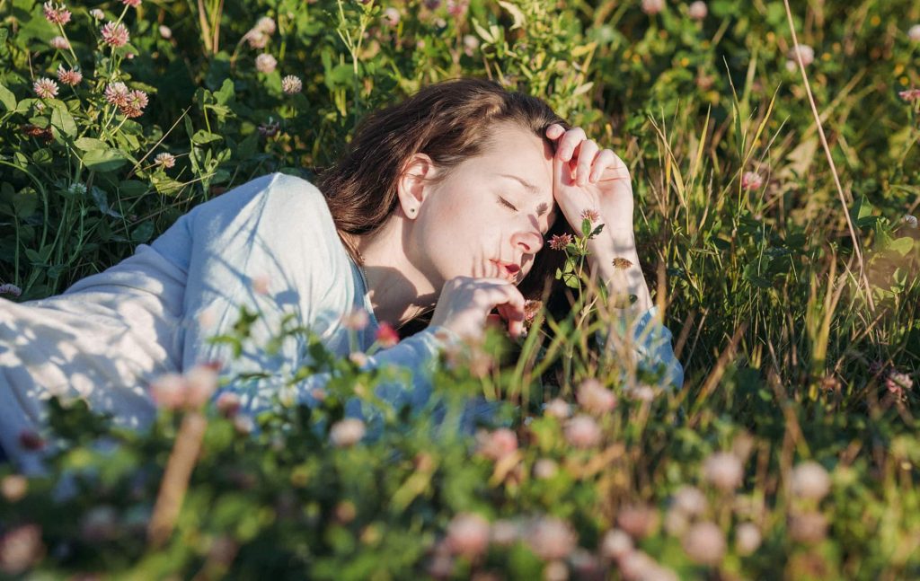 Frau liegt im Gras und riecht an Blume