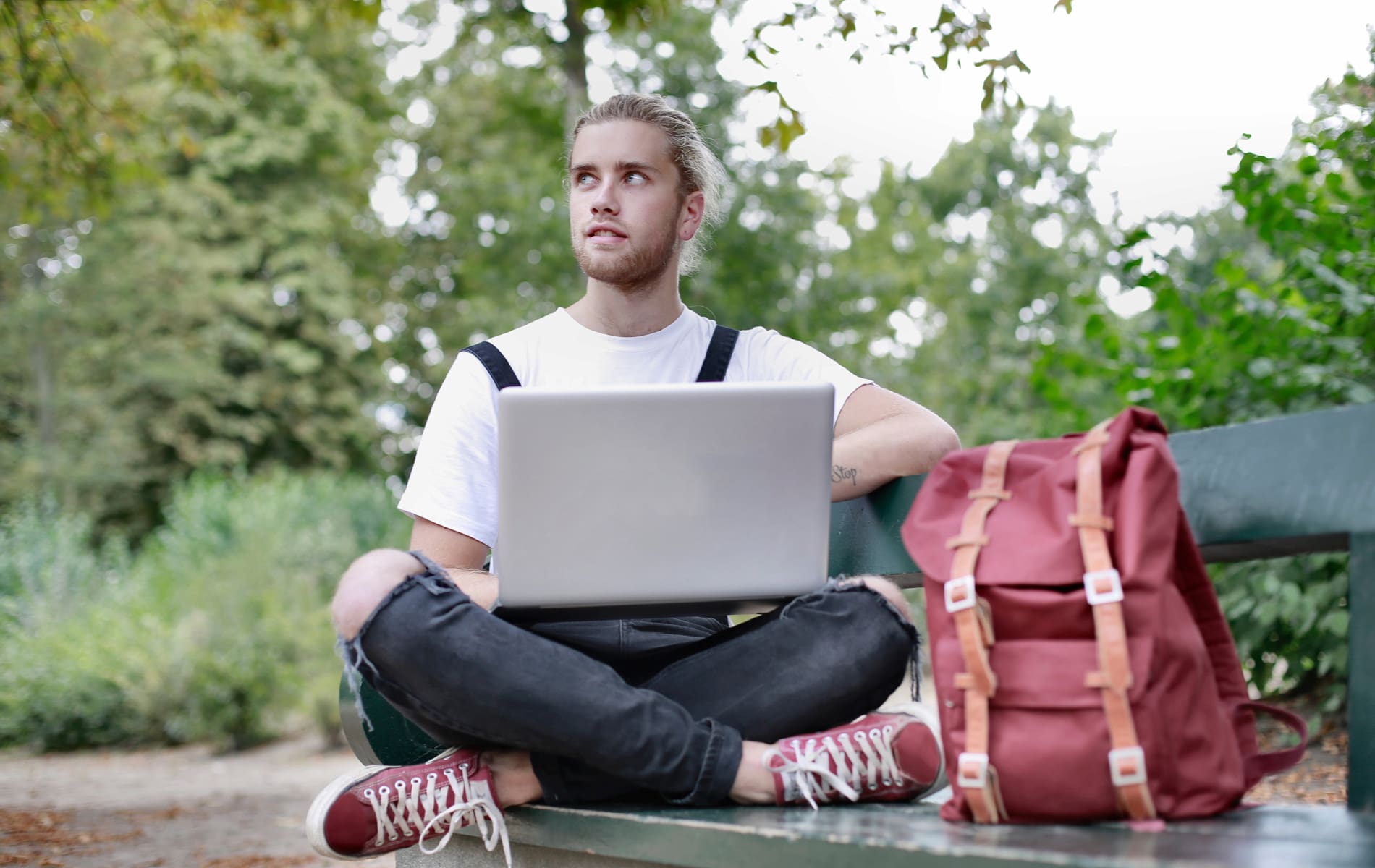 Mann mit Laptop und Rucksack sitzt auf Bank