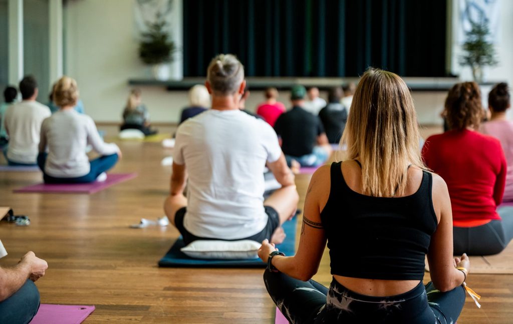 Menschen sitzen im Schneidersitz auf Yogamatten