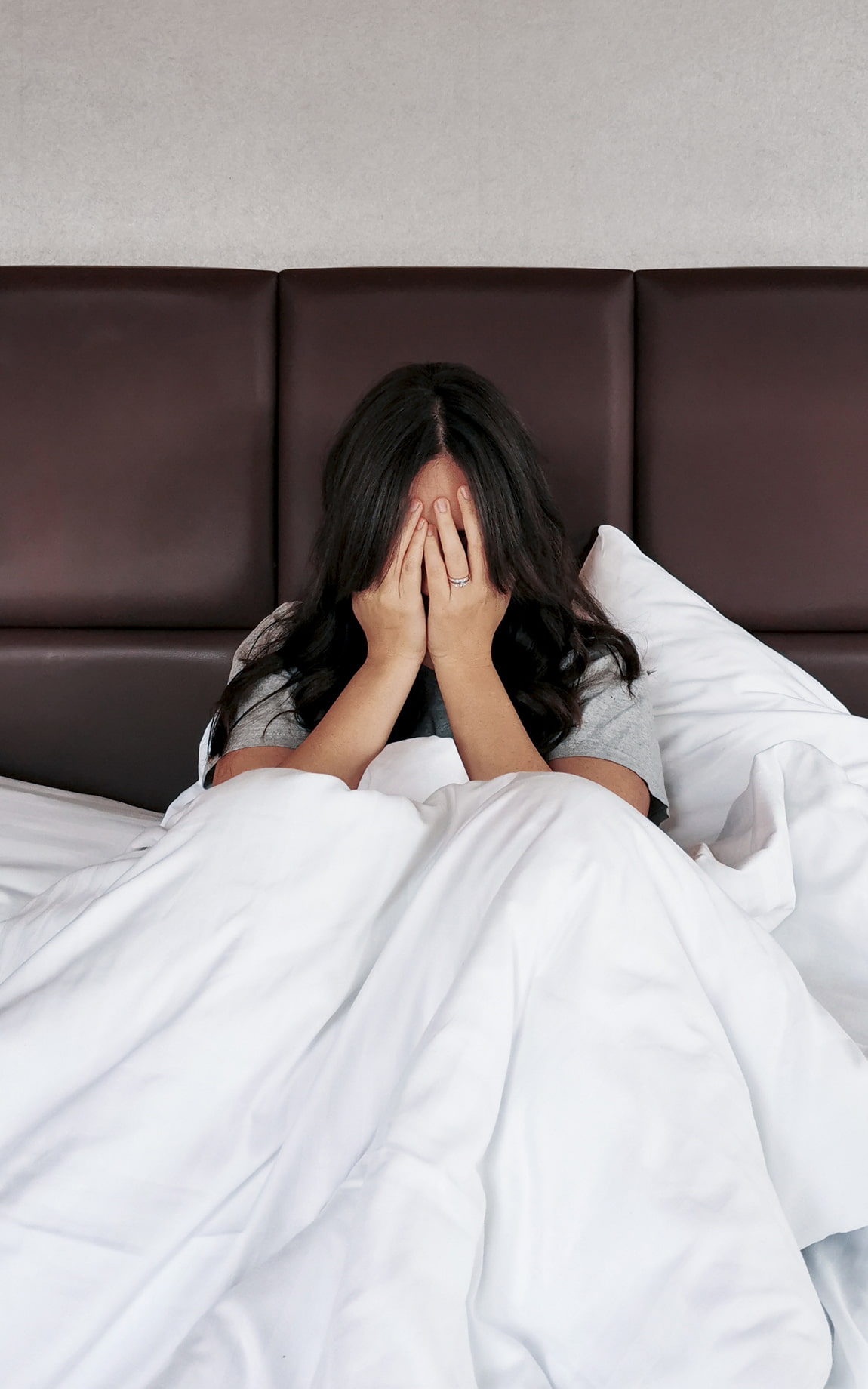 Junge Frau sitzt mit Händen vor Gesicht im Bett | Biohacking BD
