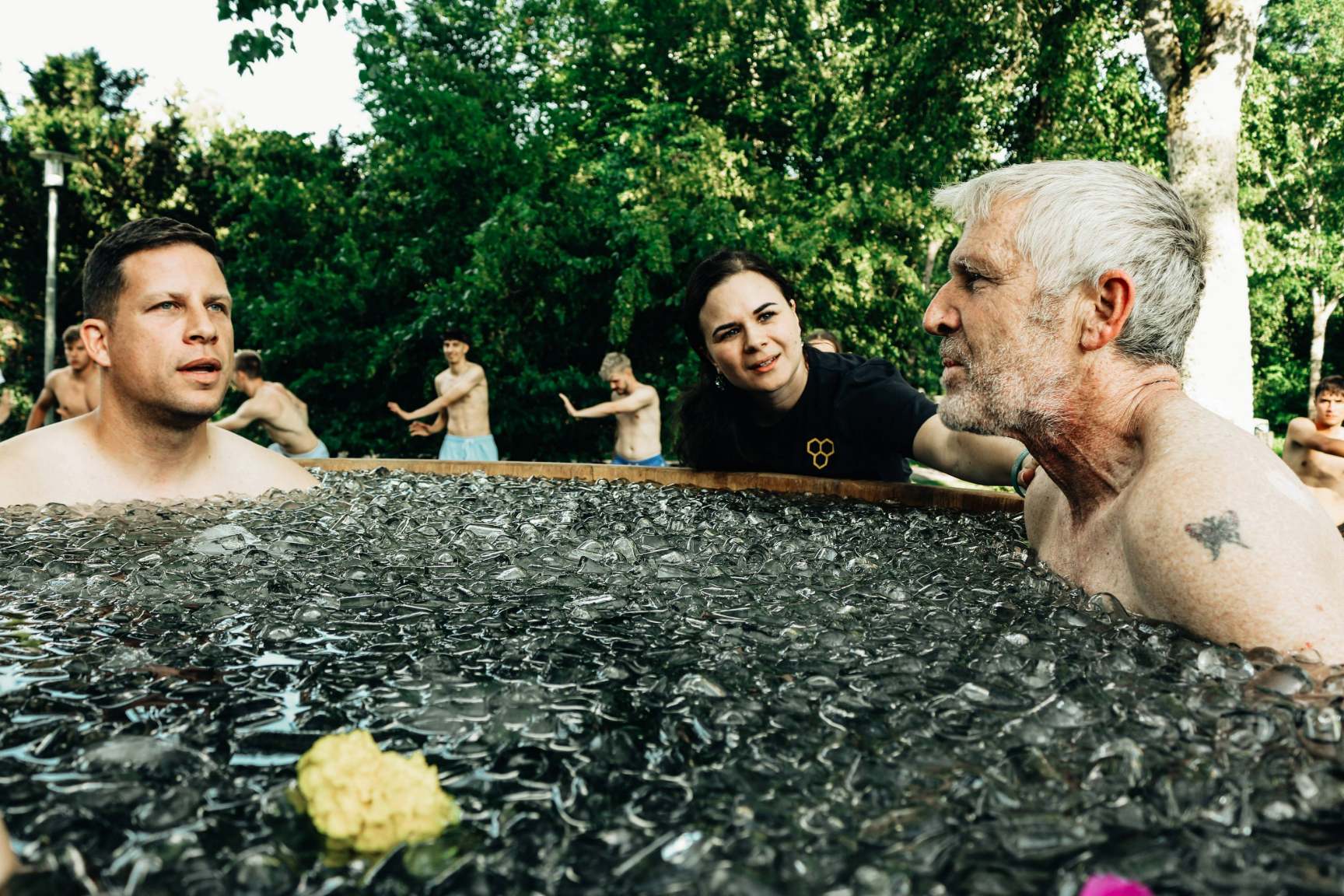 Zwei Männer die im Eisbad sitzen und von einer Frau begleitet werden