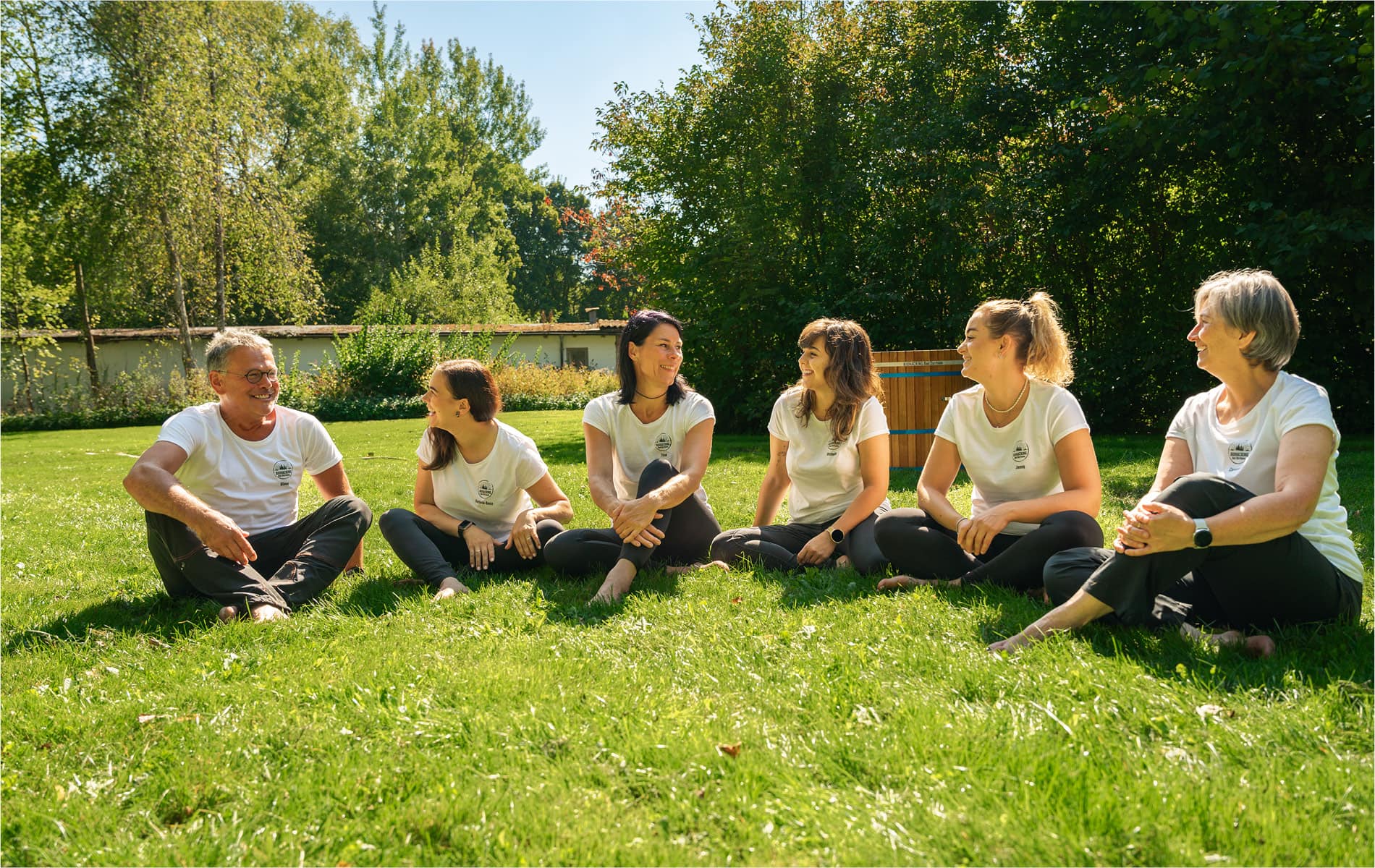 6 Personen sitzen lachend im Gras